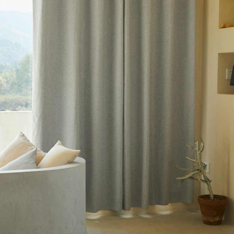 Cortinas Cortinas grises colgando junto a un sillón y una planta en maceta.